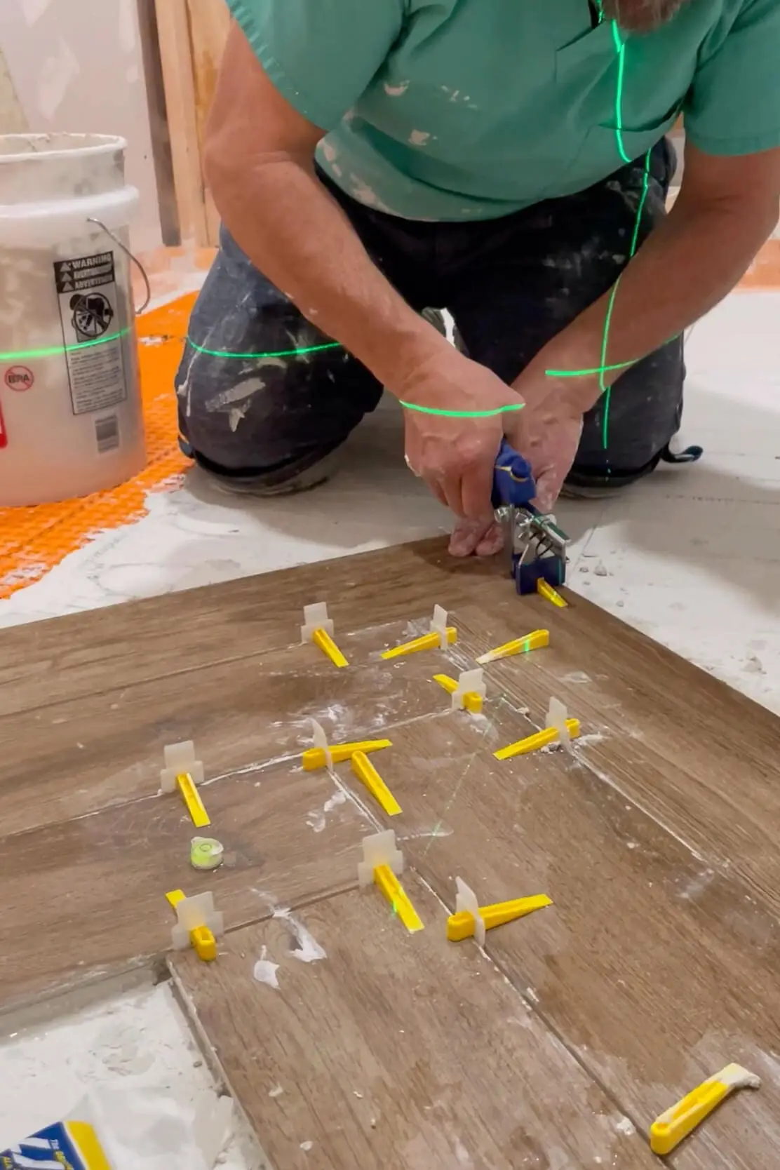 Close-up of a worker using tile leveling tools and spacers on wood-look tiles to achieve a perfectly aligned bathroom floor design.